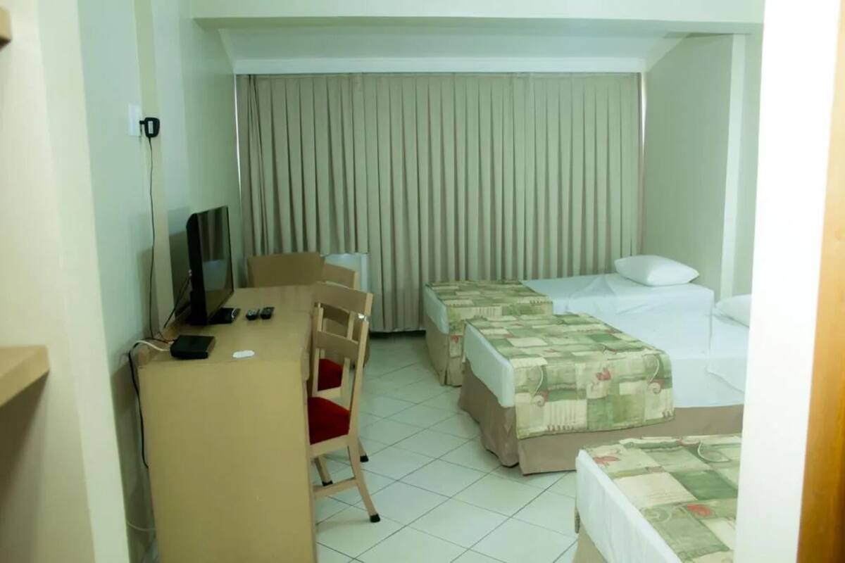 A hotel room with a desk, two beds, a chair, and a television.