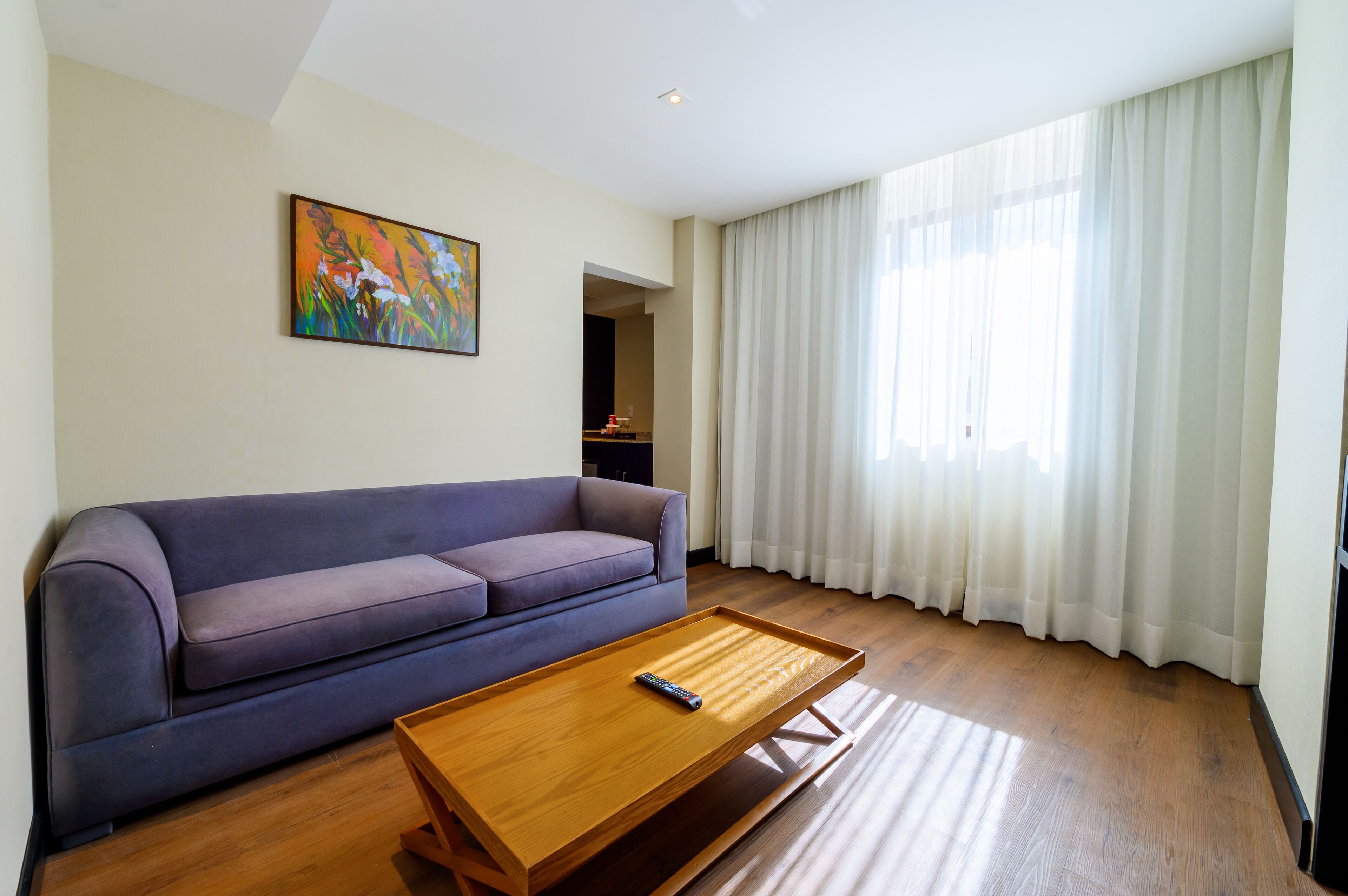 A modern living room with a sofa, a wooden coffee table, and a painting on the wall.