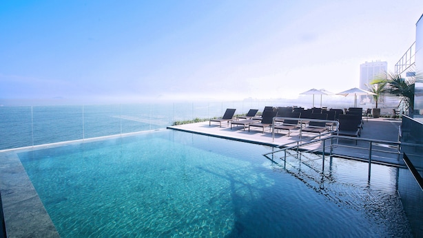 Una piscina infinita con agua azul cristalina, sillones de descanso, sombrillas y vista al océano.