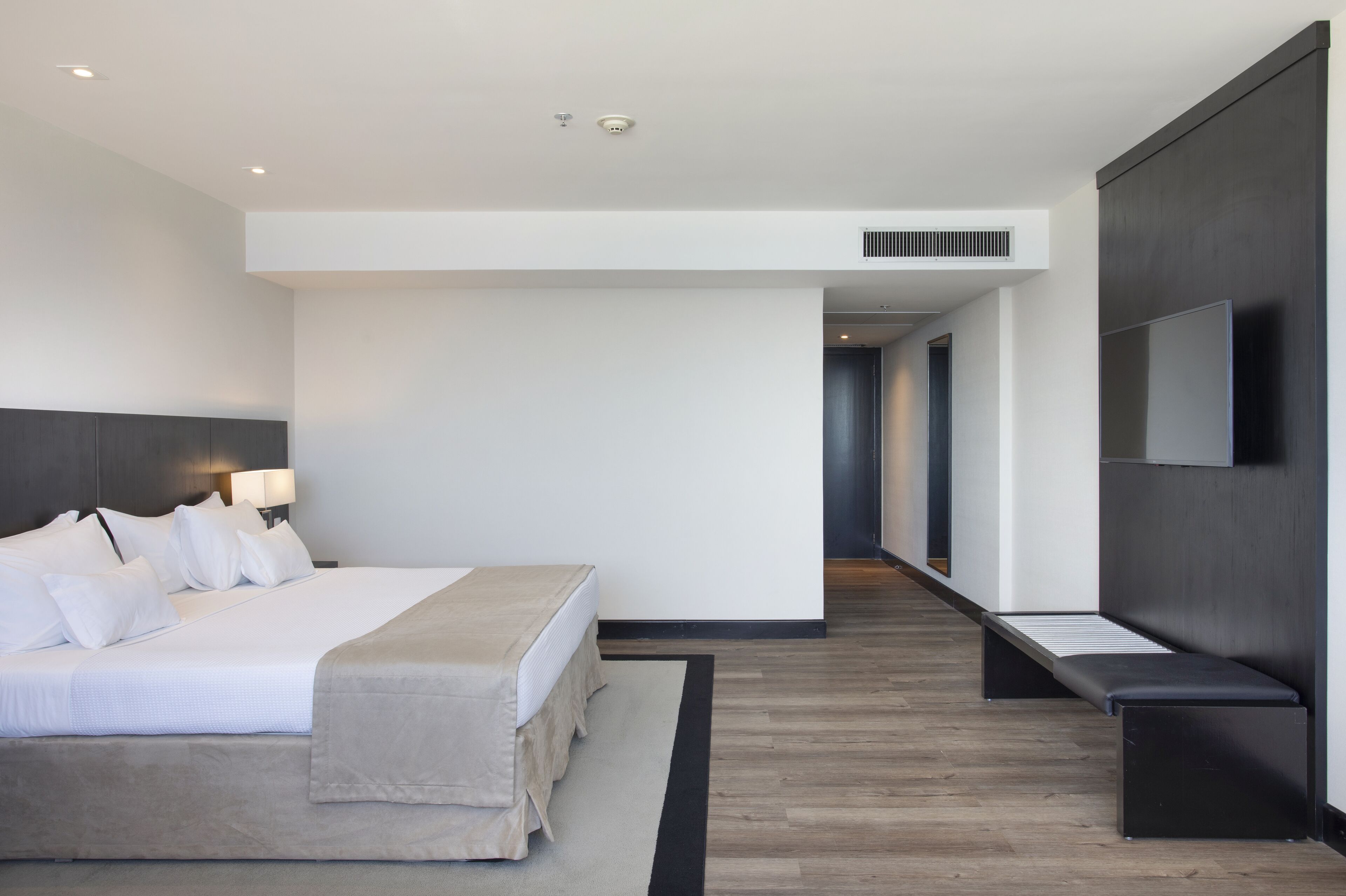 A modern hotel room with a large bed, bedside tables, a flat-screen TV, and a walk-in closet.