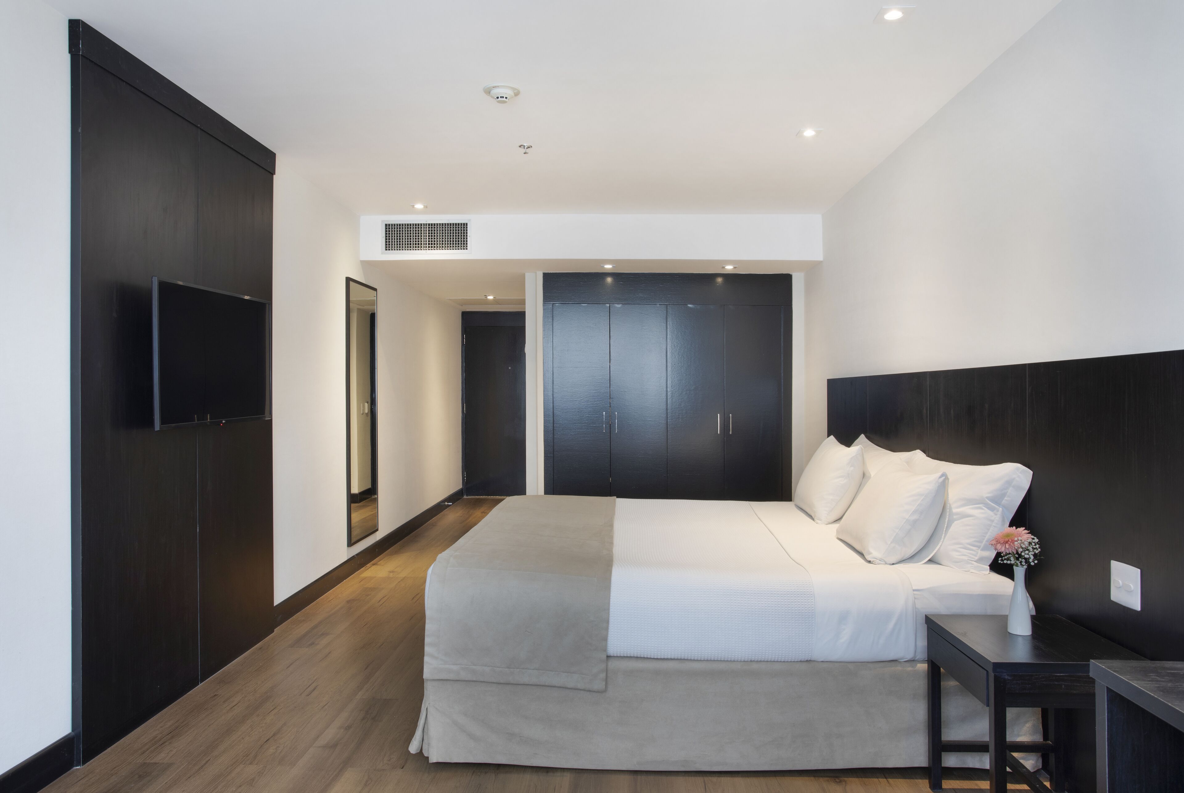 Un dormitorio moderno con una cama grande, un armario de madera oscura y un televisor de pantalla plana.