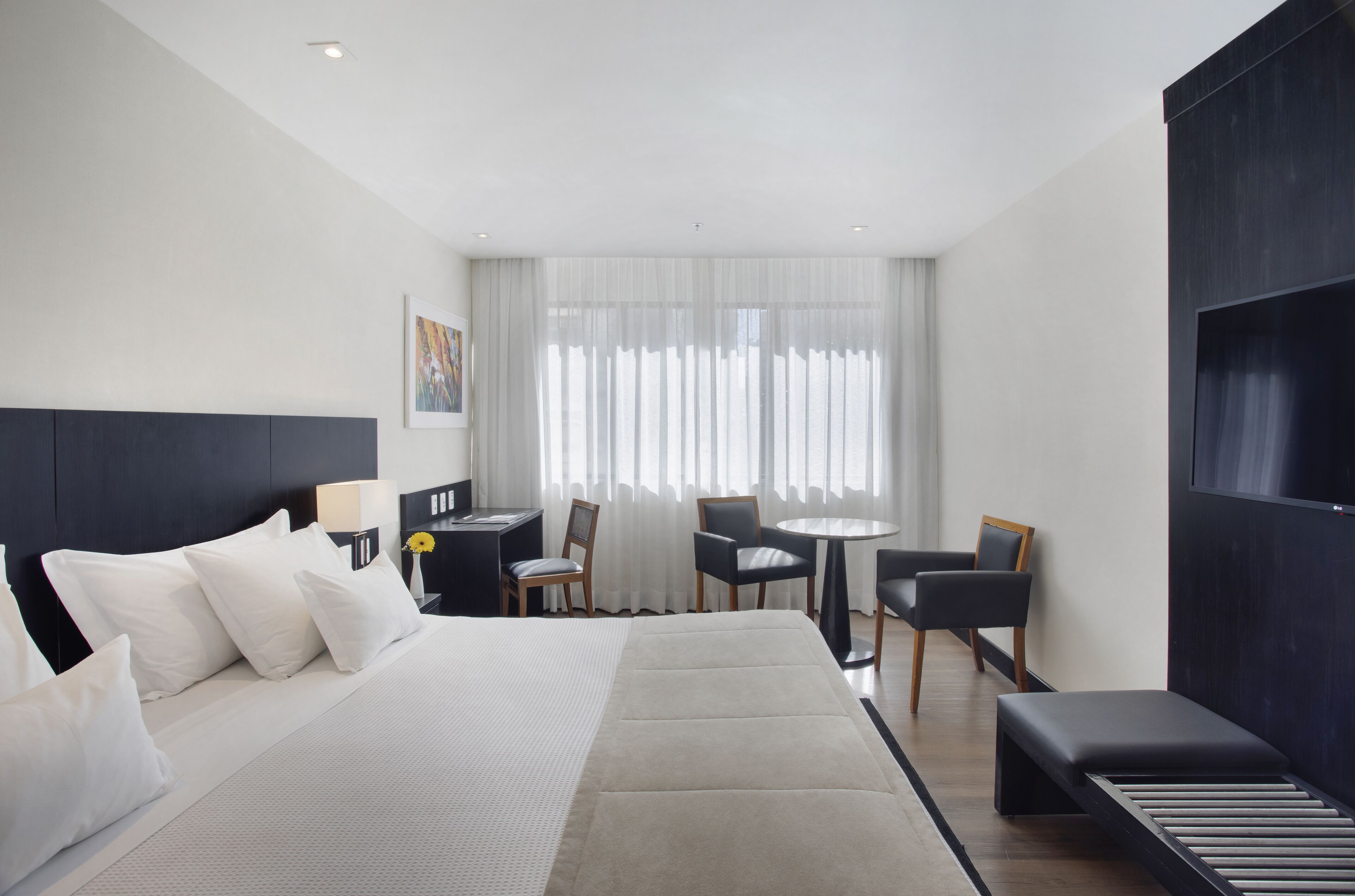 Een moderne hotelkamer met een groot bed, een bureau met stoel, een kleine ronde tafel met twee stoelen, en een bank.