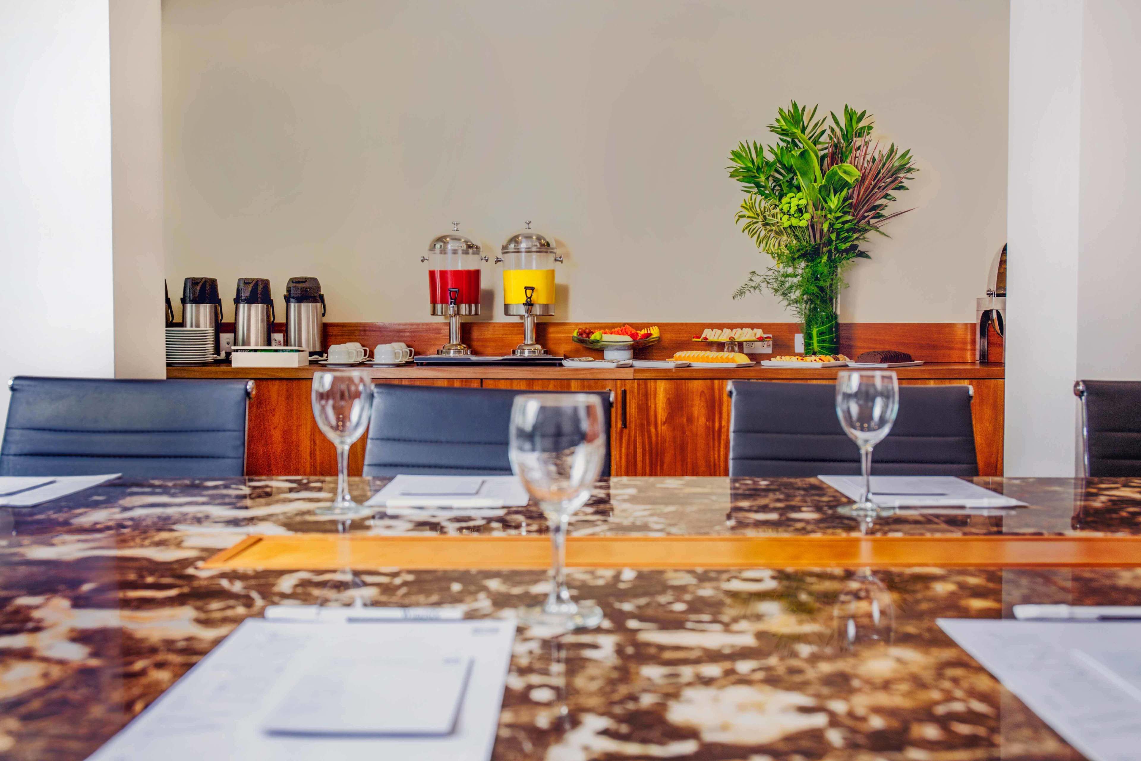 Un comedor con una mesa de mármol, dos copas de vino y una barra de desayuno con cafeteras y una exhibición de frutas.