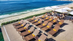 Un área de descanso frente a la playa con tumbonas y sombrillas, con vista al océano y la playa.