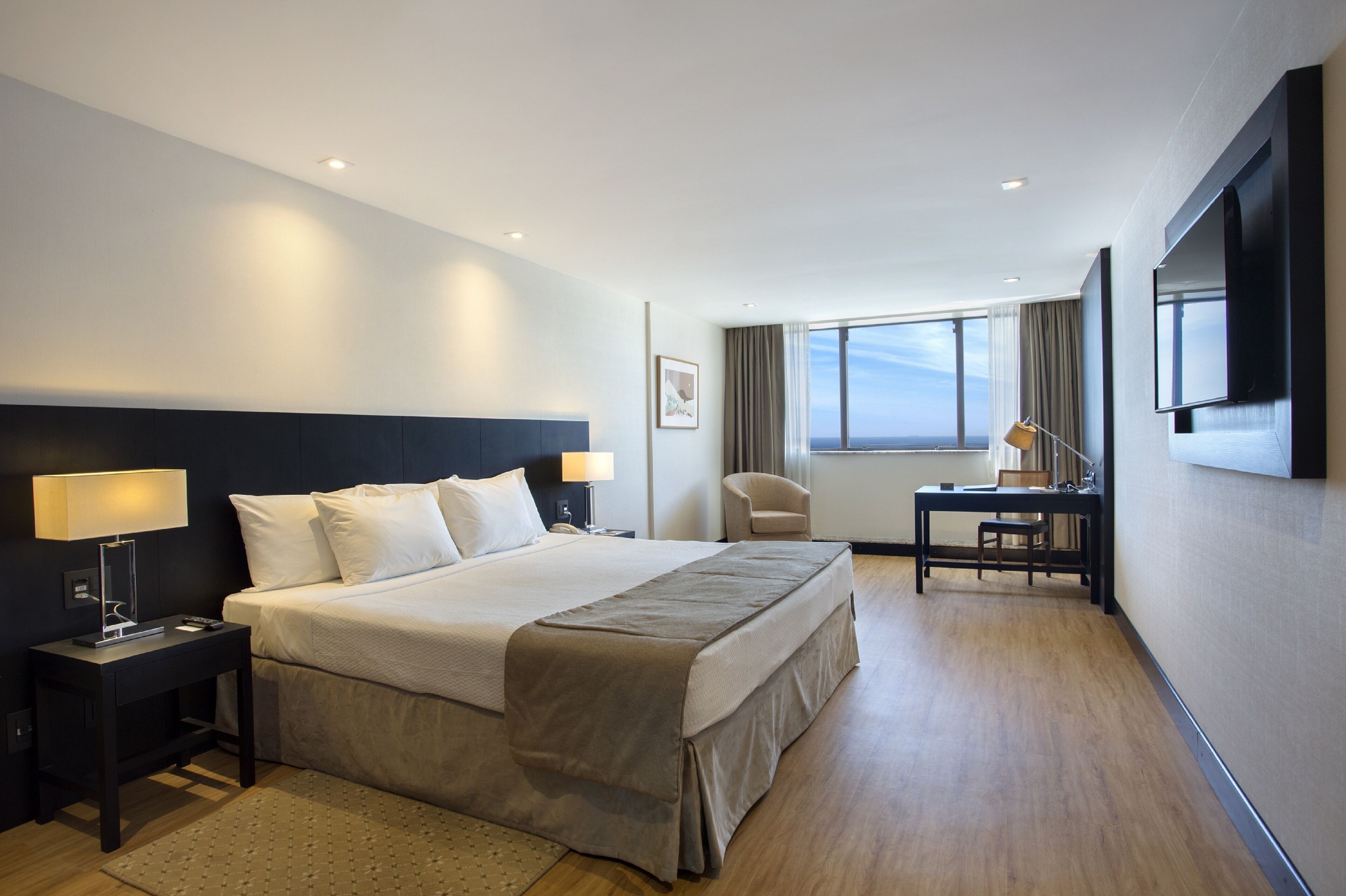 A modern hotel room with a large bed, bedside tables, a desk, and a TV.