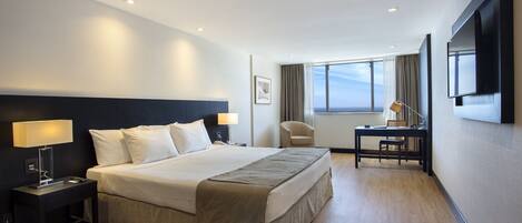 A modern hotel room with a large bed, bedside tables, a desk, and a TV.