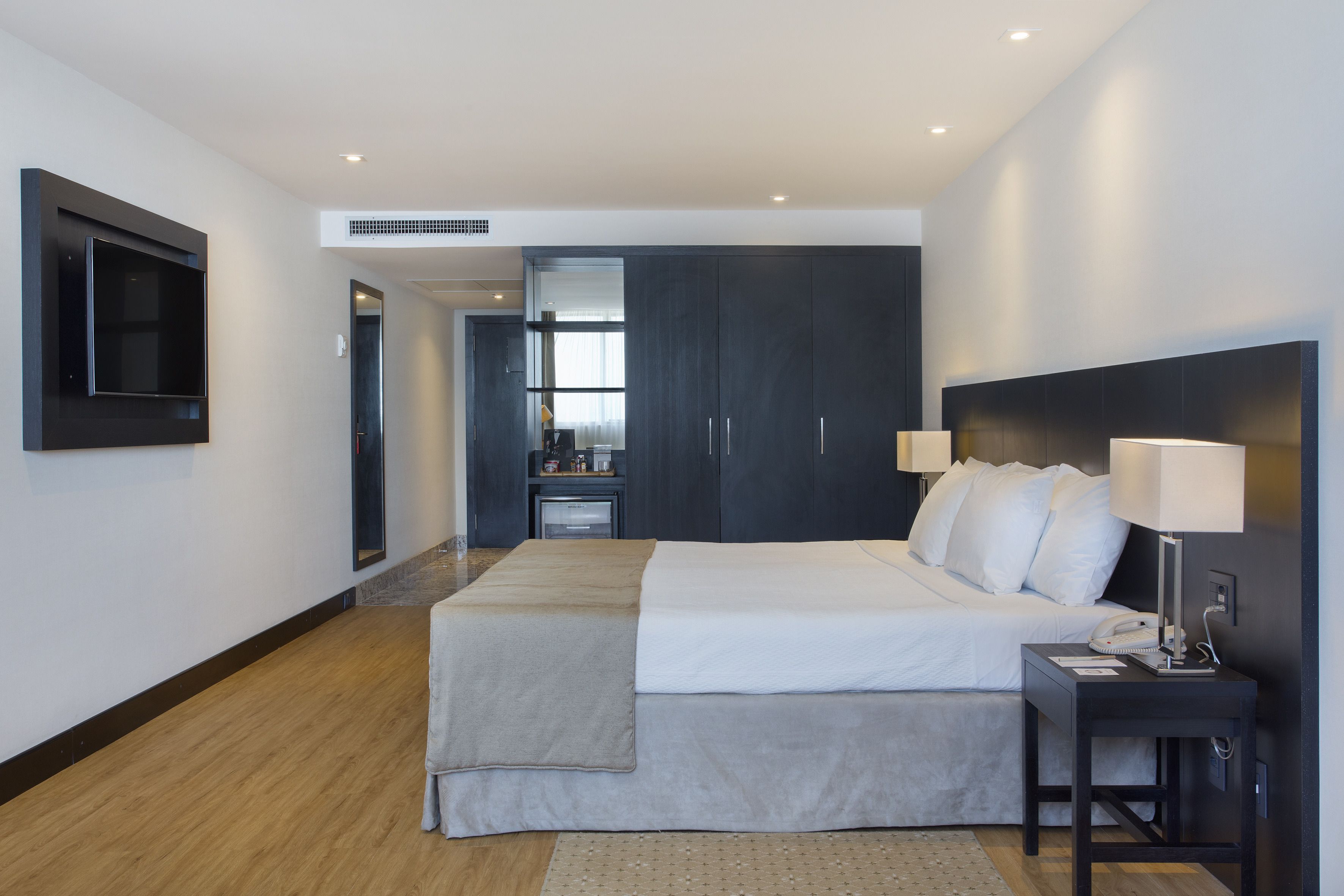A modern hotel room with a large bed, bedside lamps, a TV, and a desk with a phone and lamp.