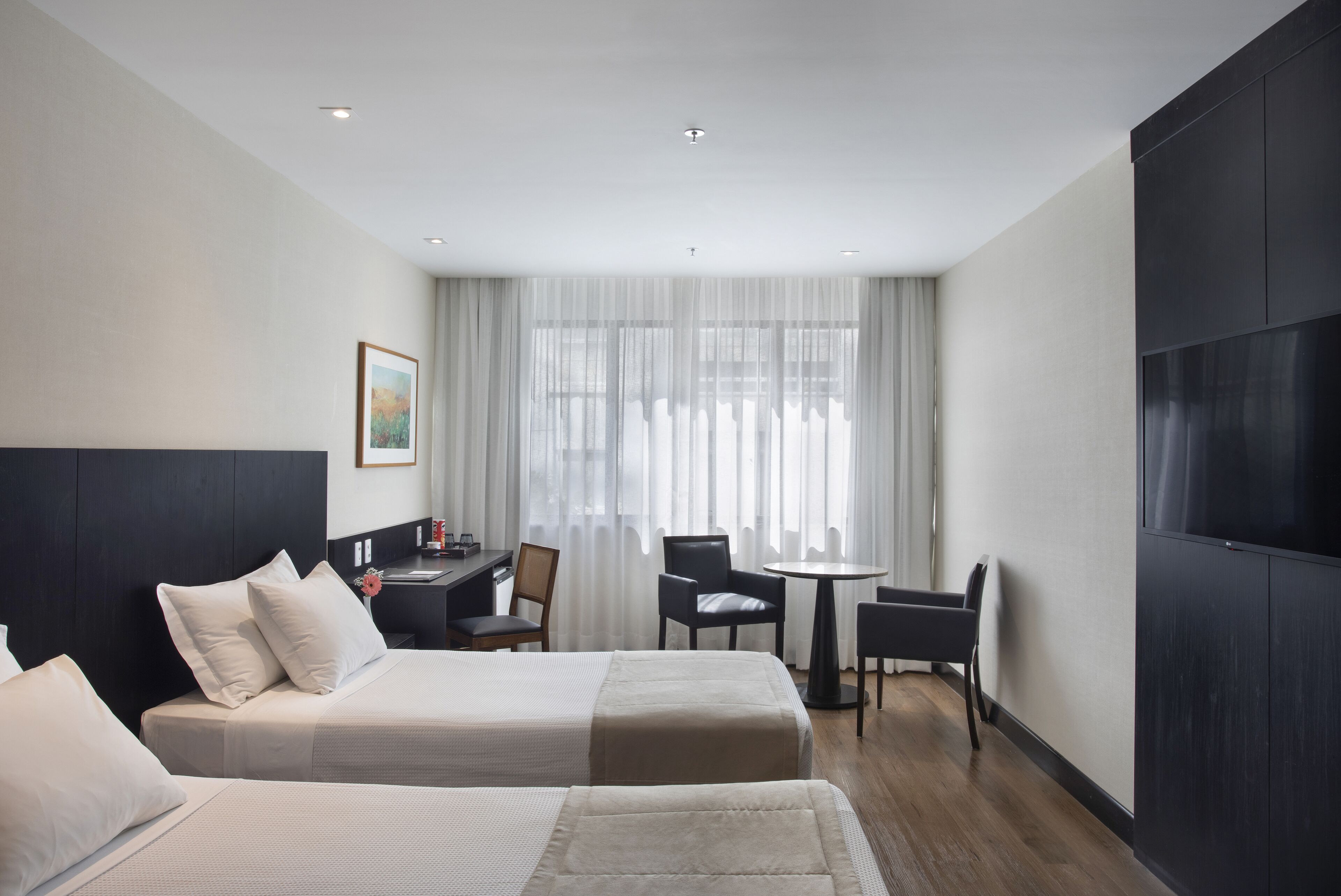 A hotel room with two beds, a desk, a chair, a small table, and a TV.