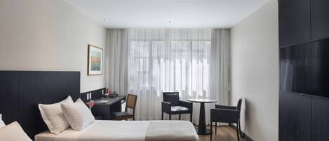 A hotel room with two beds, a desk, a chair, a small table, and a TV.
