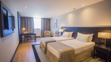 A hotel room with two beds, a desk, a chair, a TV, and a window with curtains.