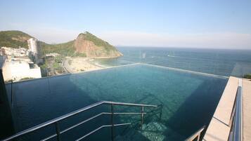 Vista despejada de una piscina con barandilla metálica, que domina una playa y un paisaje montañoso.