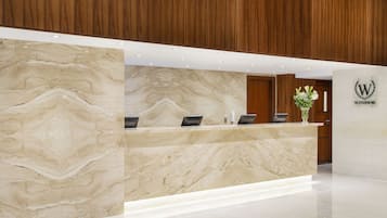 A reception desk with a marble finish, a logo, and a vase with flowers.
