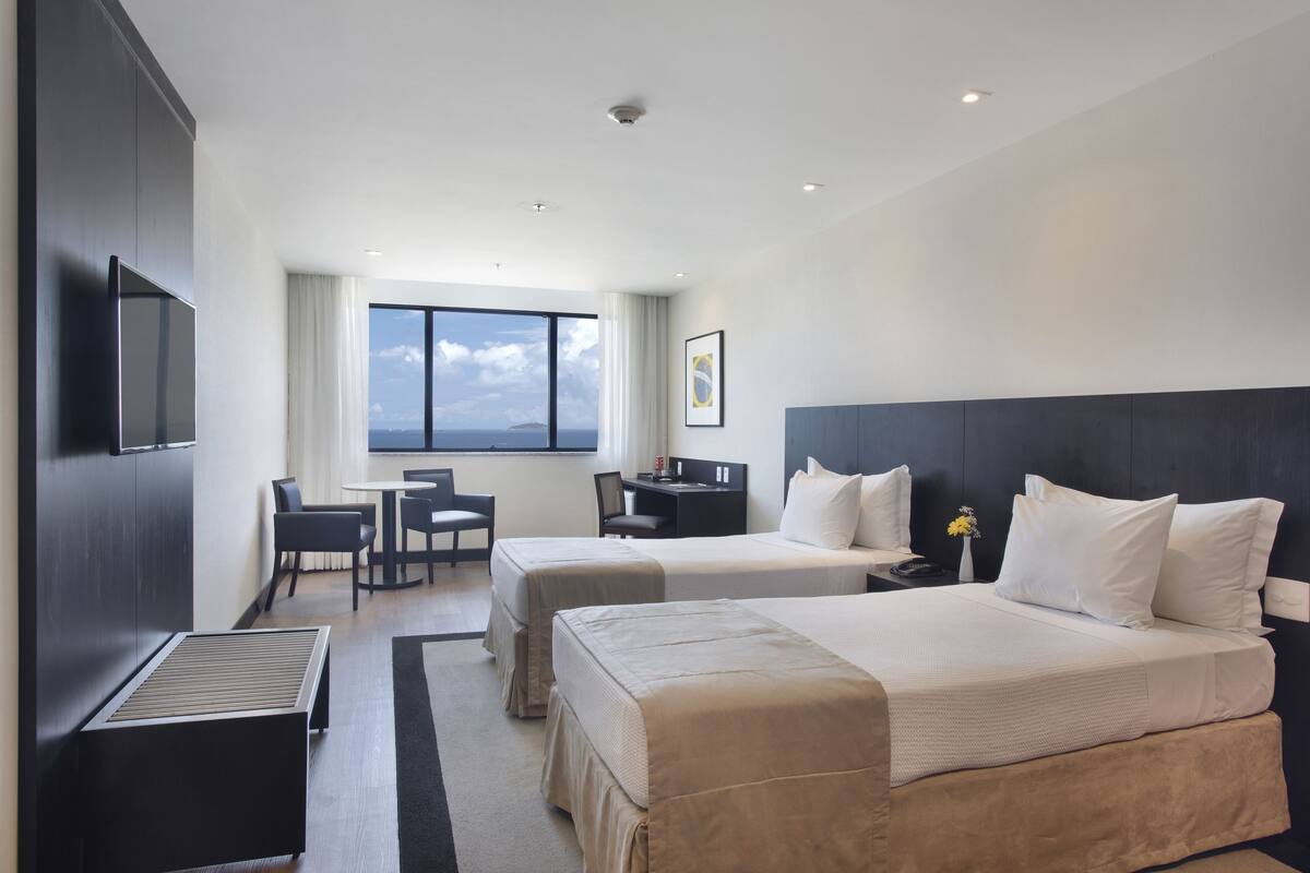 Habitación de hotel con dos camas, un escritorio, una silla y un ventanal que ofrece vistas.