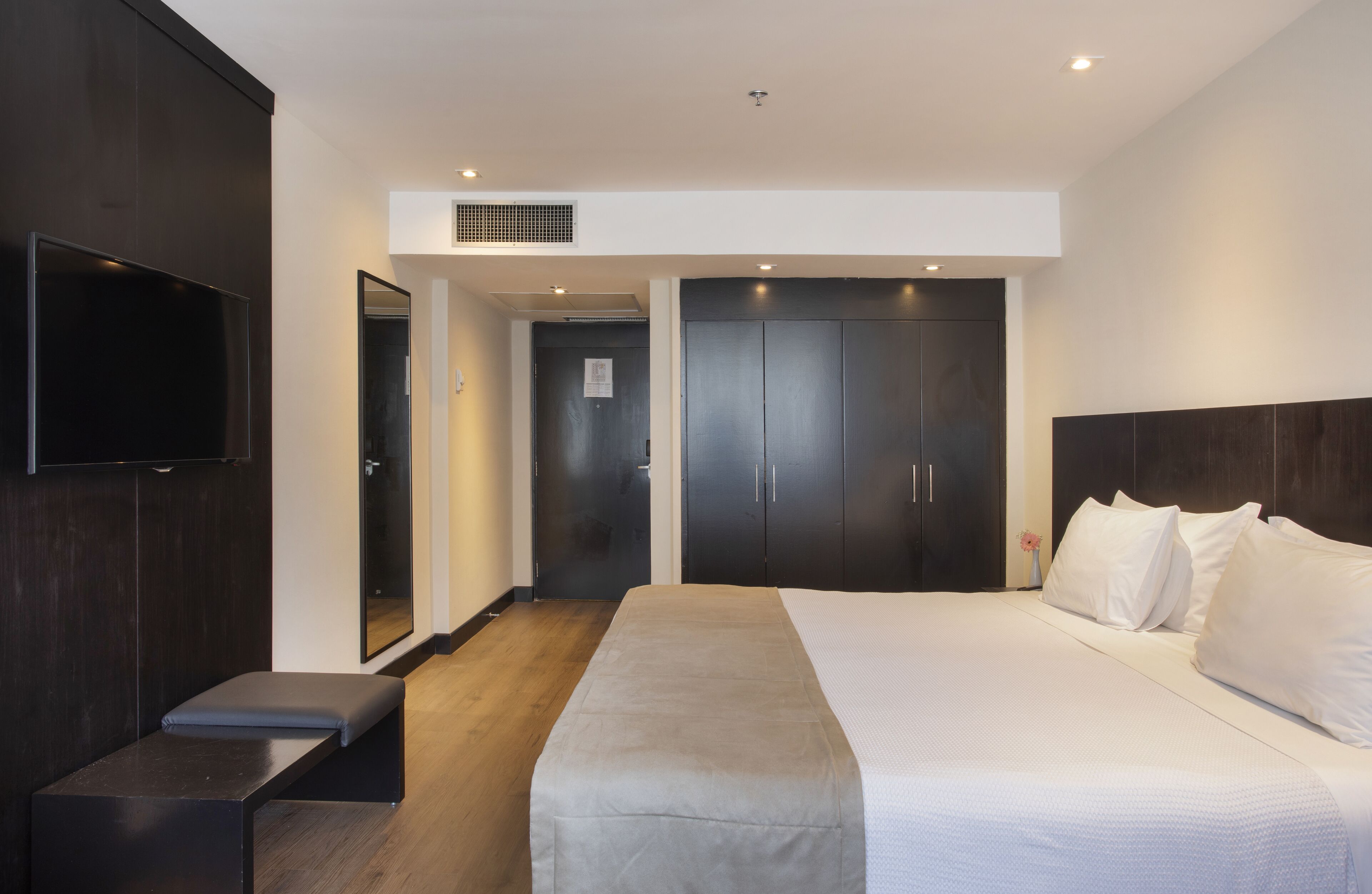 Ein modernes Hotelzimmer mit einem großen Bett, einem Flachbildfernseher, einer Sitzbank und einem Kleiderschrank.