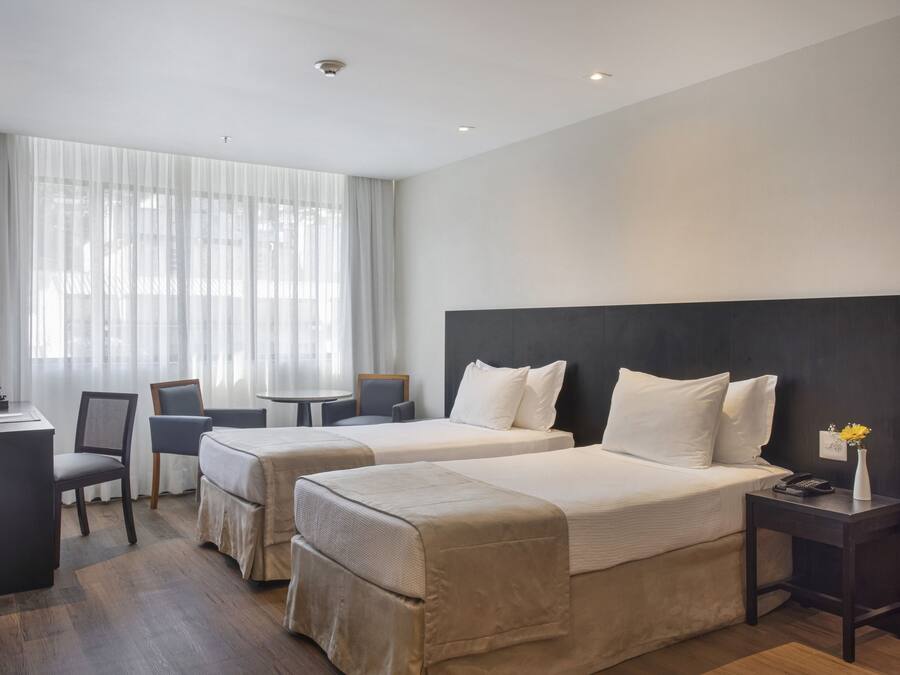 Habitación de hotel con dos camas, un escritorio, sillas y una mesita.