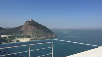 Visão nítida de uma piscina com grade de metal, praia e montanha ao fundo.