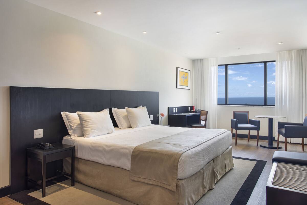 Habitación de hotel moderna con una cama grande, un escritorio y vistas al océano.