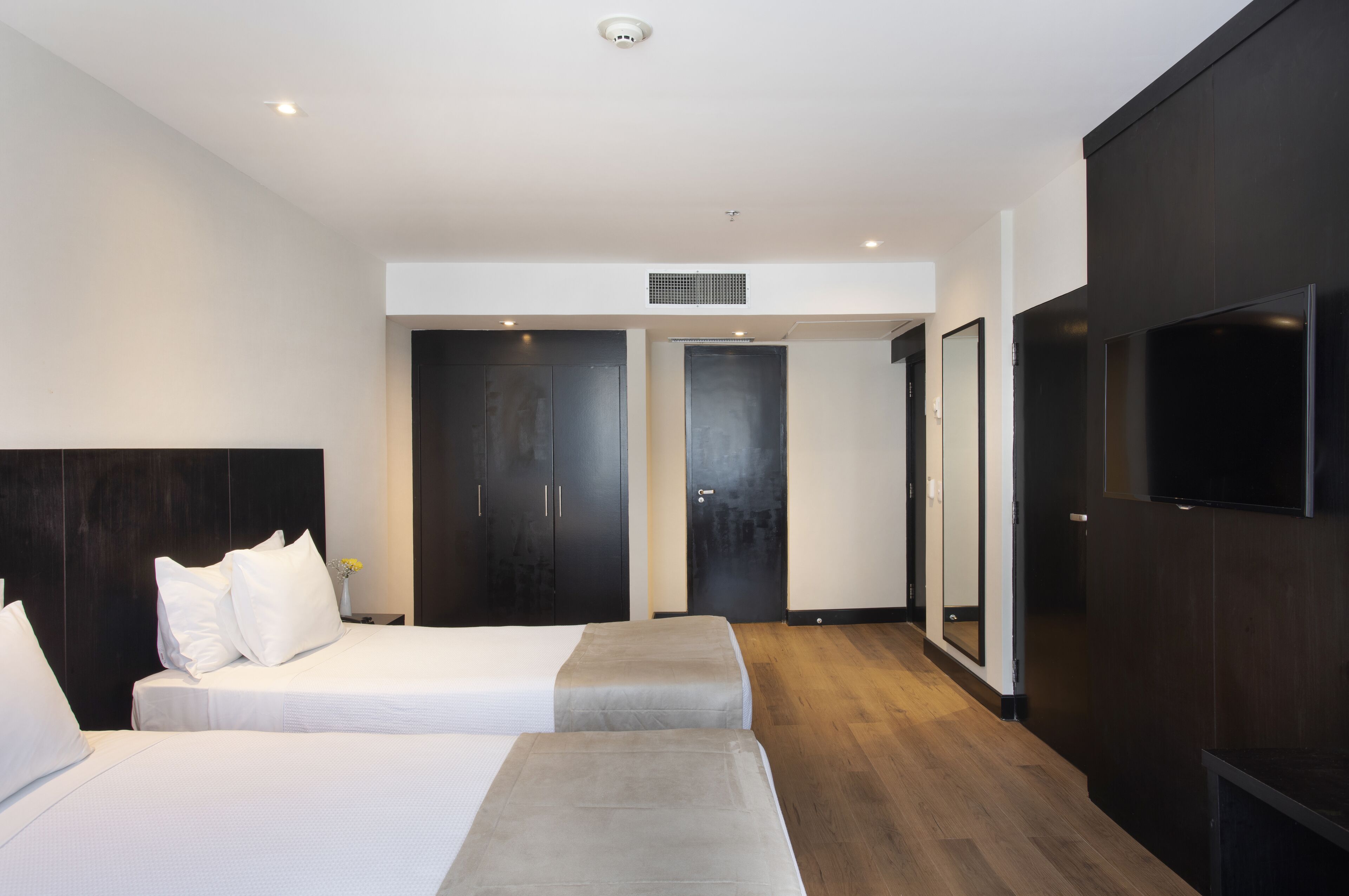 Quarto de hotel moderno com duas camas, uma televisão de tela plana e um espelho grande.