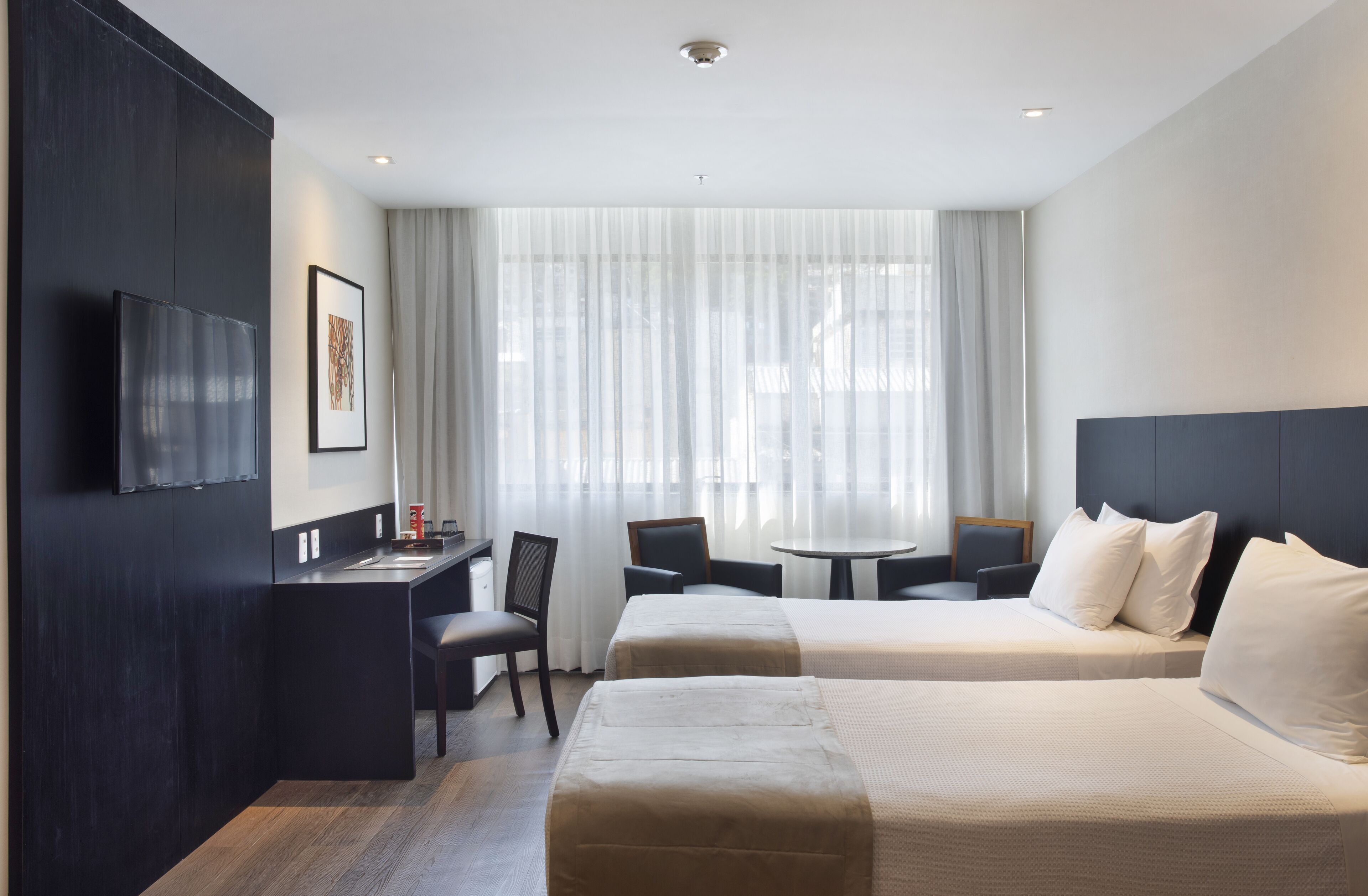 Quarto de hotel com cama, escrivaninha e cadeira.