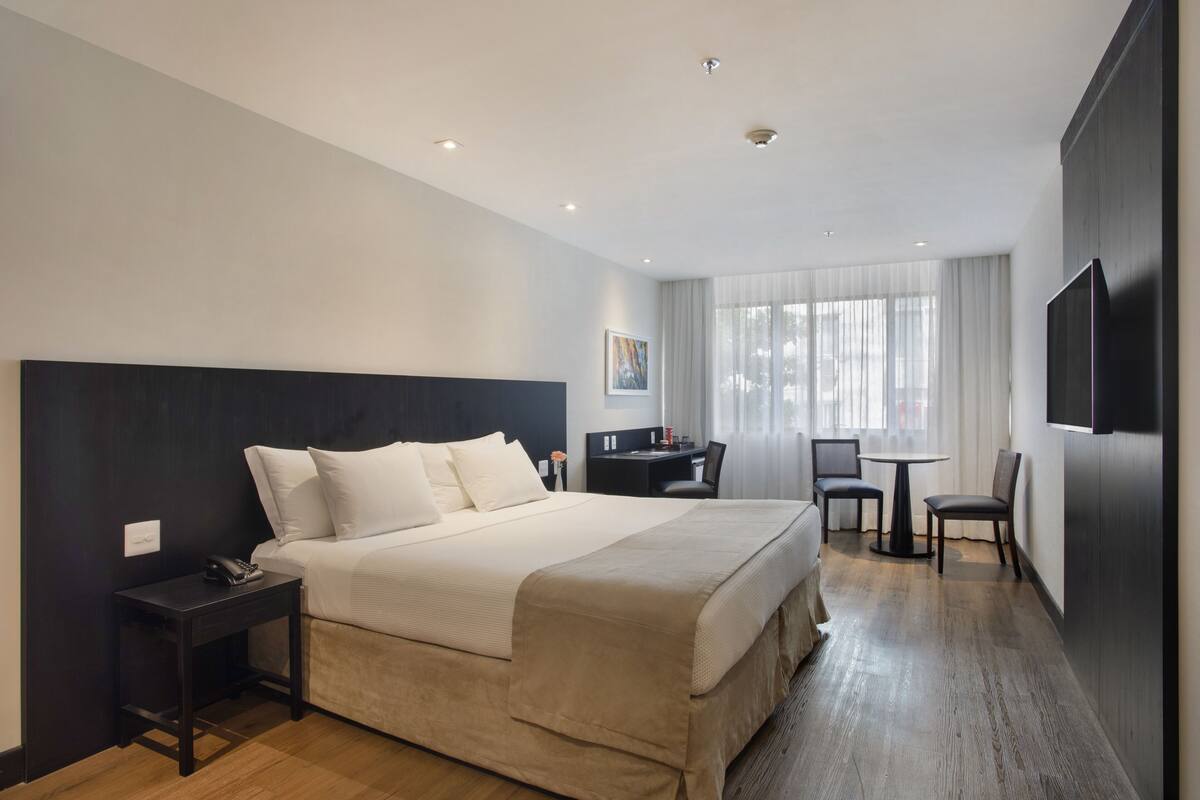 Una habitación de hotel moderna con una cama grande, mesitas de noche, escritorio, sillas y televisión.