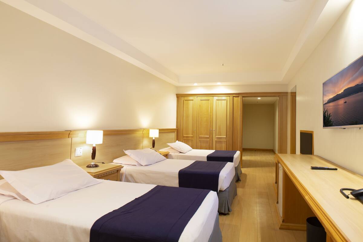 A hotel room with two beds, a desk, a chair, a TV, and a wardrobe.