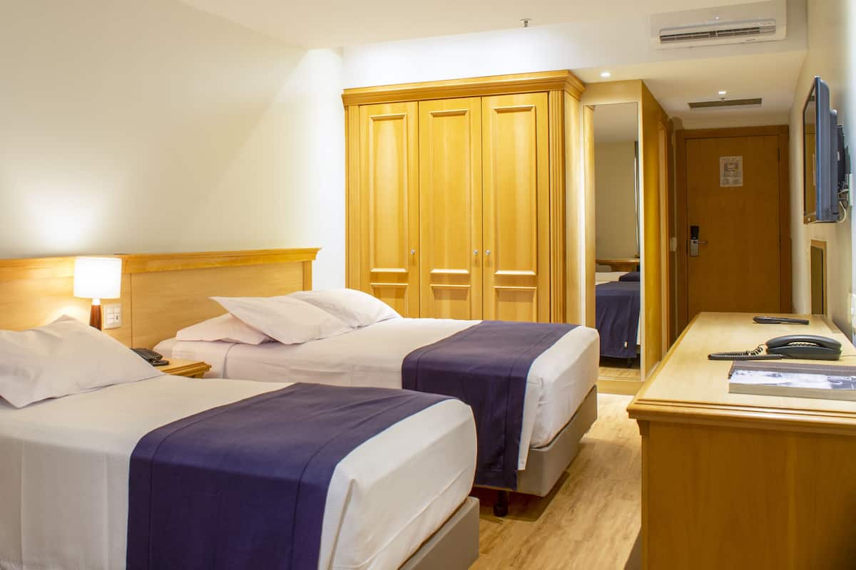 A hotel room with two beds, a desk with a chair, a wardrobe, and a television.