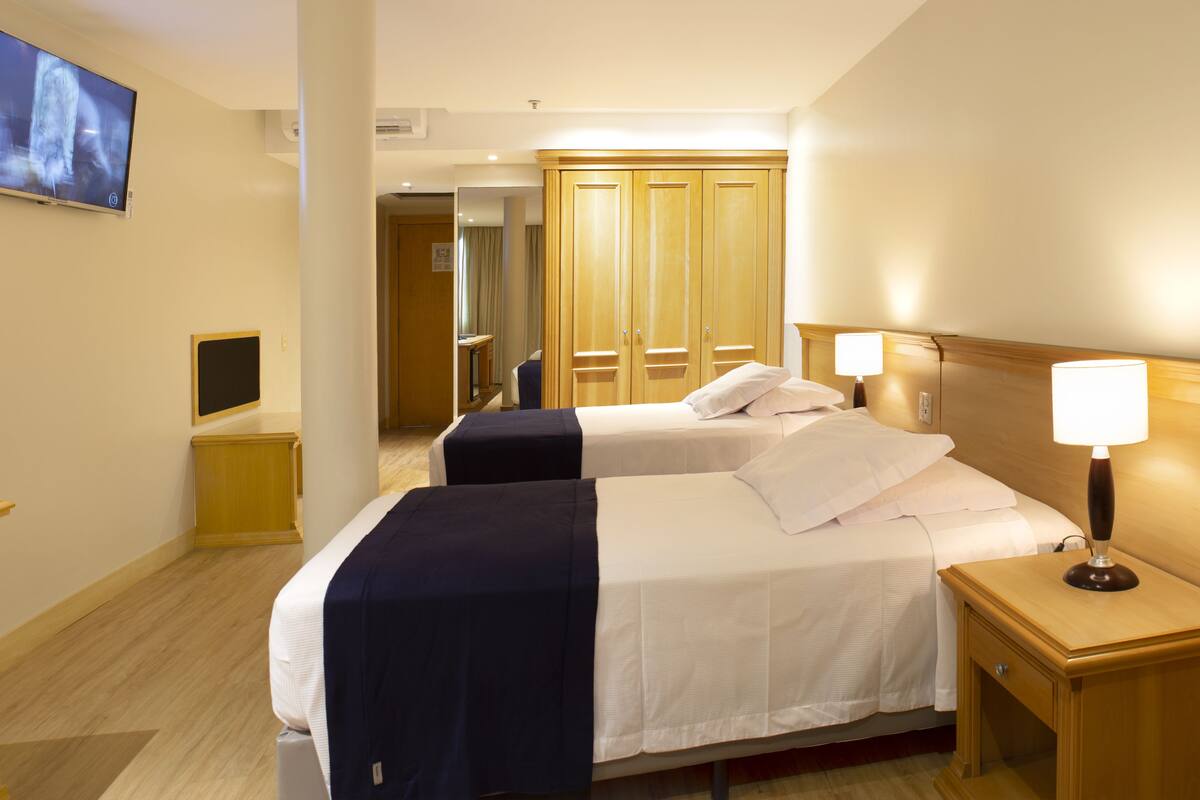 A hotel room with two beds, a TV, a desk, and a wardrobe.