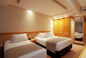 Une chambre d’hôtel avec deux lits, une armoire en bois, une table de chevet et un miroir.