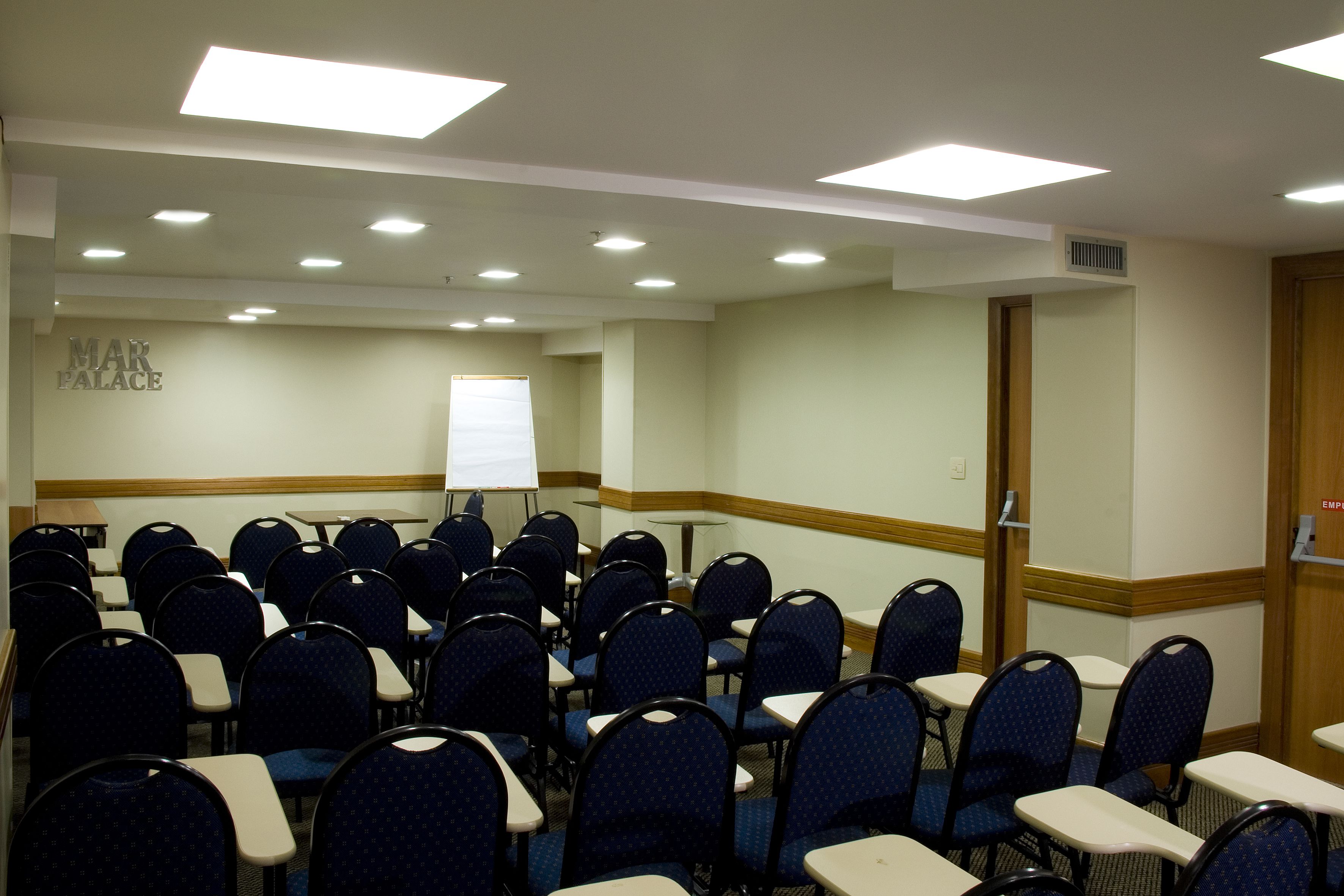Konferenssihuone, jossa on riveissä tuoleja ja pöytiä, valkotaulu ja kyltti, jossa lukee: ”MAR PALACE”.