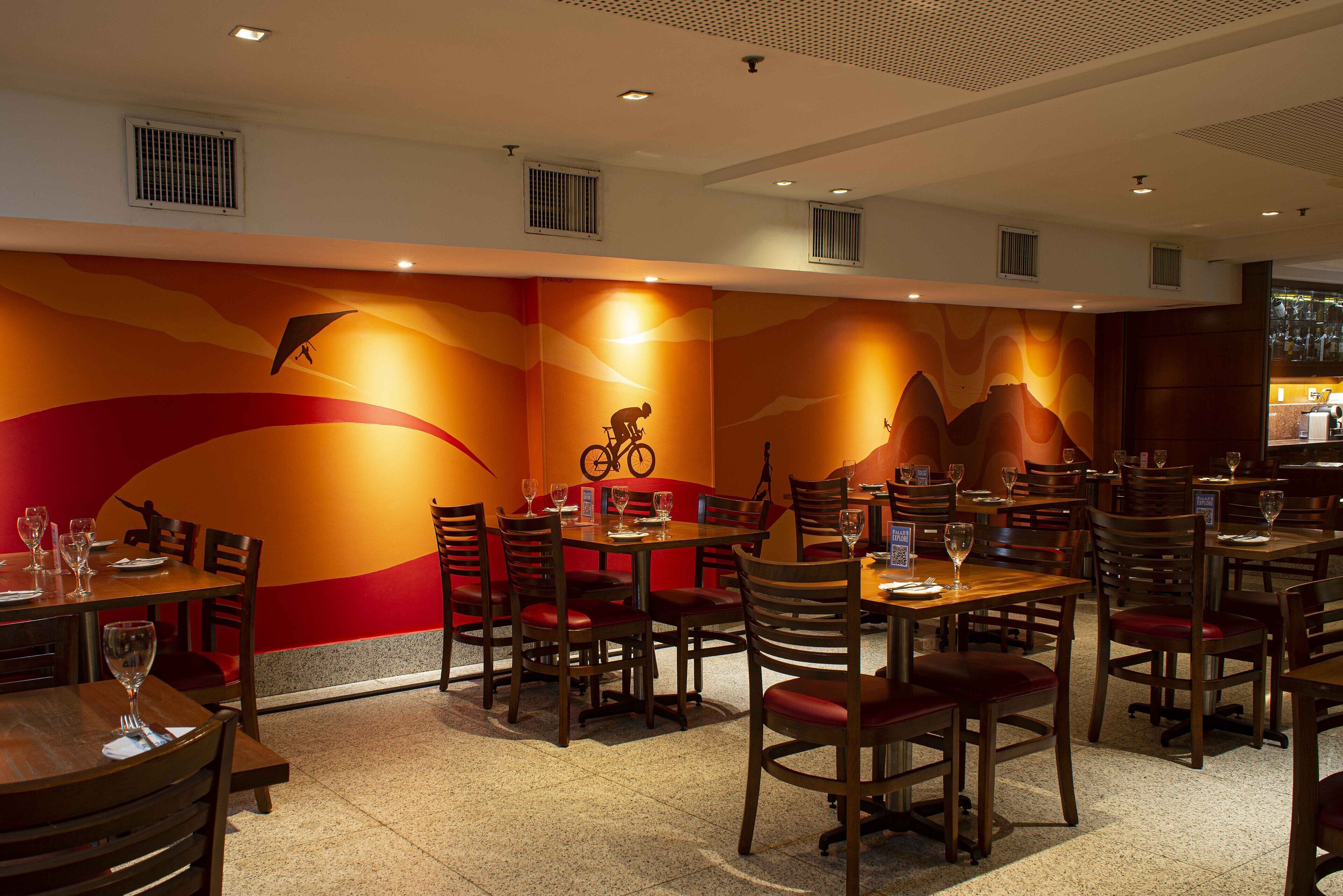 A restaurant with multiple tables and chairs, a mural on the wall, and a ceiling with ventilation.