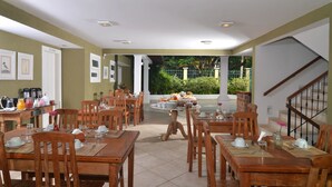 A dining area with wooden tables and chairs, a buffet table with food and drinks, and a staircase leading to an upper level. - Pousada dos Buzios (Búzios)
