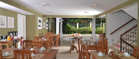 A dining area with wooden tables and chairs, a buffet table with food and drinks, and a staircase leading to an upper level.