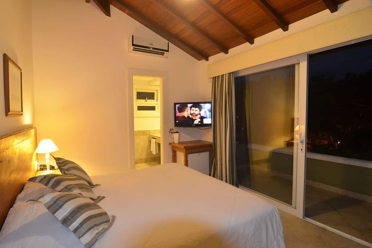 A hotel room with a bed, a television, a nightstand, a lamp, a sliding glass door, and a ceiling fan.