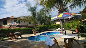 A swimming pool with stone tiles, lounge chairs, and umbrellas. - Pousada dos Buzios (Búzios)