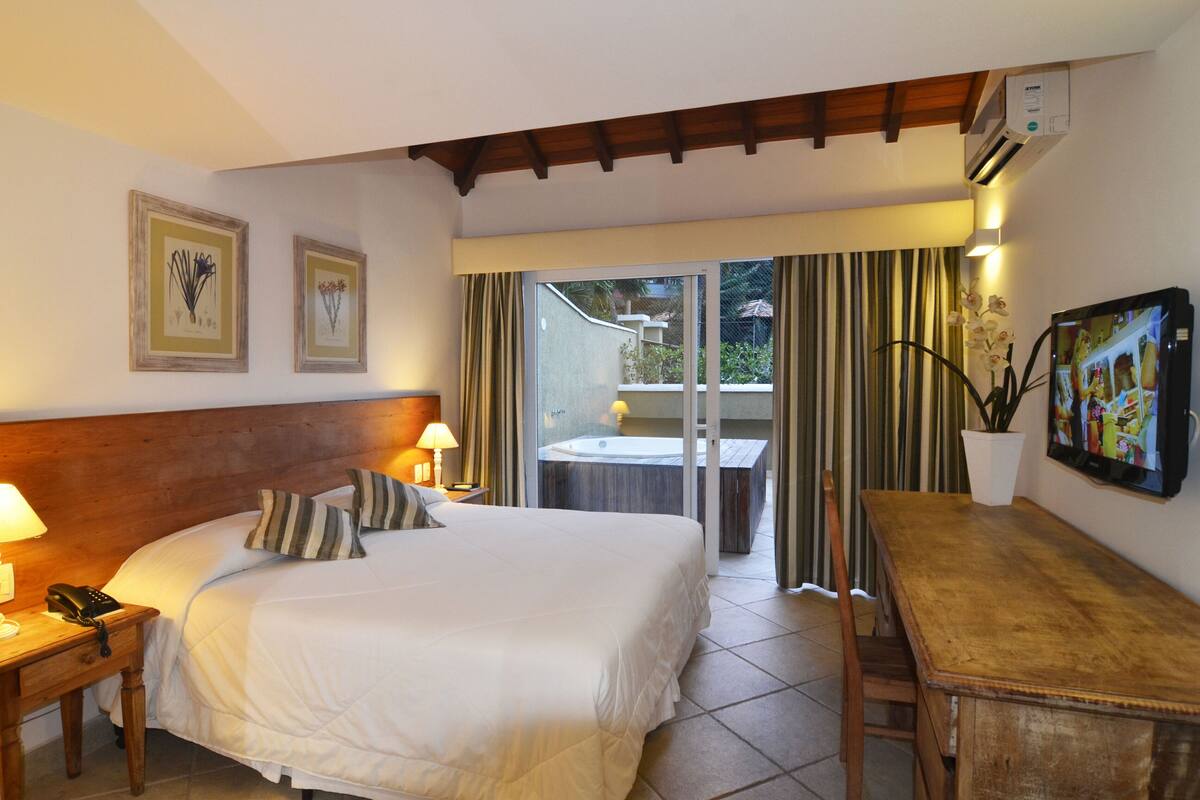 A hotel room with a bed, bedside table, lamp, and a view of a balcony with curtains.