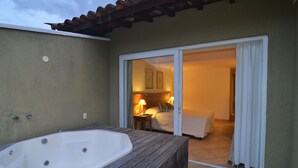 A spa area with a large hot tub and a sliding glass door leading to a bedroom with a bed and a nightstand. - Pousada dos Buzios (Búzios)