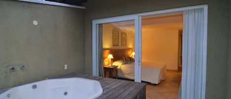 A spa area with a large hot tub and a sliding glass door leading to a bedroom with a bed and a nightstand.