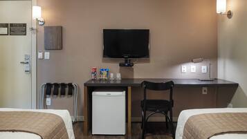 Habitación de hotel con cama, escritorio con televisor, refrigerador, silla y lámpara fijada a la pared.