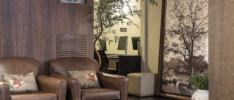 A living room with two leather armchairs, a small table with a magazine, a large framed picture of a tree, and a potted plant.