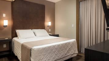 Habitación de hotel con una cama grande, dos lámparas de noche, un cabecero de madera, un escritorio y una ventana con cortinas.