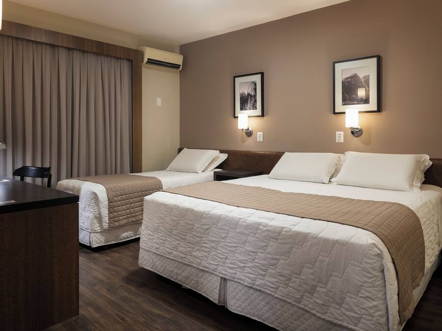 Habitación de hotel con dos camas, un escritorio y una silla. Hay dos lámparas de pared y dos cuadros en la pared.