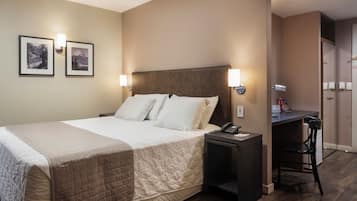 A hotel room with a large bed, bedside tables, a desk with a chair, and two framed pictures on the wall.