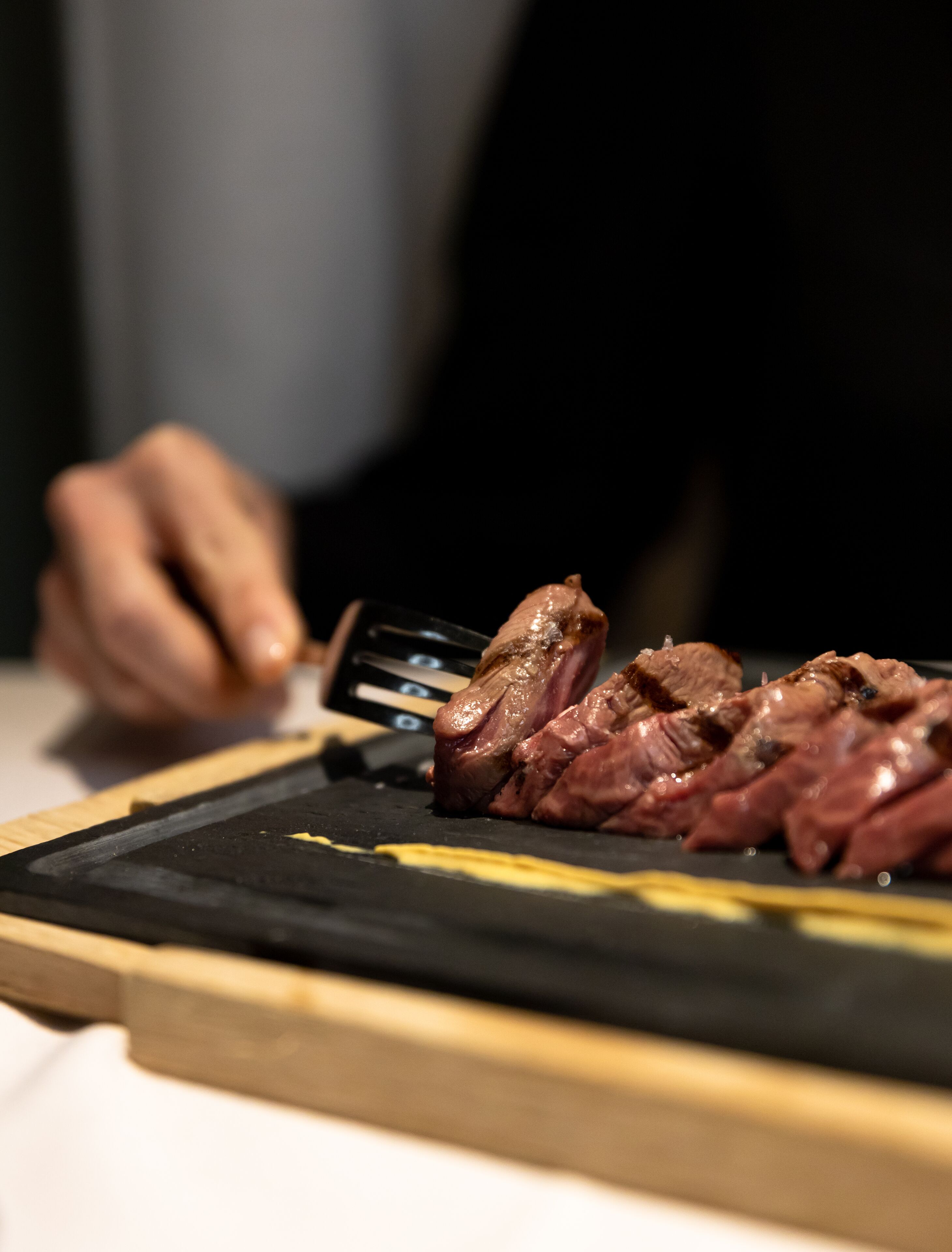 A person slicing meat on a black cutting board.
