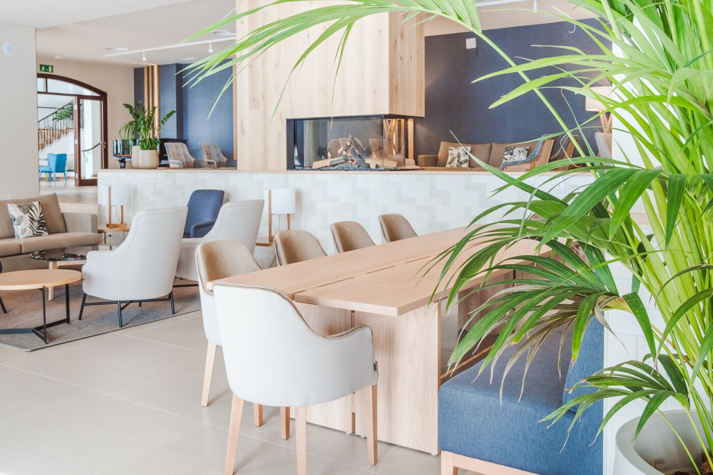 A modern living room with a wooden dining table, white sofas, and a large potted plant.