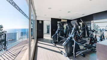 Ein Fitnessraum mit Trainingsgeräten, ein Balkon mit Meerblick und ein modernes Interieur.