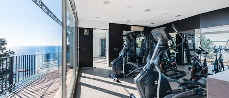 A gym with exercise equipment, a balcony with a view of the sea, and a modern interior design.