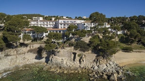 A coastal hotel with multiple floors, a rocky shoreline, and clear waters. - Park Hotel San Jorge & Spa by Escampa Hotels (Calonge)