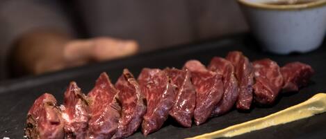A close-up of sliced meat on a black cutting board with a bowl of sauce in the background.