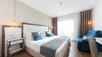 Habitación de hotel con una cama grande, un escritorio, una silla y un ventanal con cortinas.