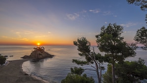 A beach with a rocky outcrop and trees in the foreground. - Park Hotel San Jorge & Spa by Escampa Hotels (Calonge)